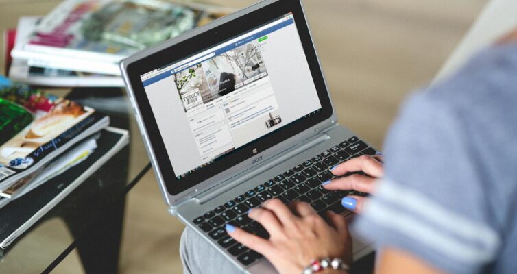 A woman typing on a laptop with social media on the screen, indoors setting.
